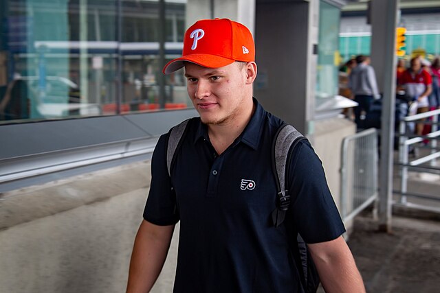 Matvei Michkov arriving at JFK Airport in New York donning Philadelphia sports apparel including a Flyers shirt and a Phillies hat.