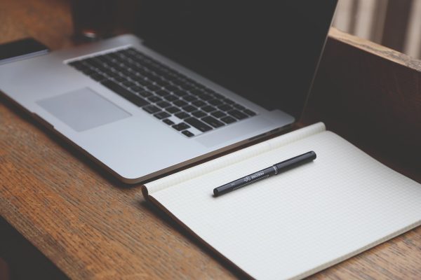 A laptop and notebook on to of a wooden desk.